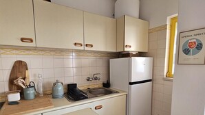 Eine Küche mit weißen Schränken, einem Kühlschrank, einer Spüle und einem Holzer Schneidebrett auf der Arbeitsfläche.