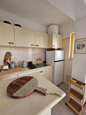 Eine Küche mit weißen Schränken, einem Kühlschrank, einer Spüle und einem Holzer Schneidebrett auf der Arbeitsfläche.