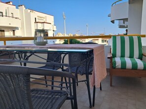 An outdoor terrace with a table and chairs, a striped cushion, and a view of buildings in the background.