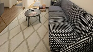 Ein Wohnzimmer mit einem gemusterten Sofa, einem Couchtisch, einem gerahmten Bild an der Wand und einer Tür zu einem anderen Raum.