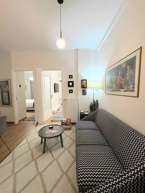 Ein Wohnzimmer mit einem gemusterten Sofa, einem Couchtisch, einem gerahmten Bild an der Wand und einer Tür zu einem anderen Raum.
