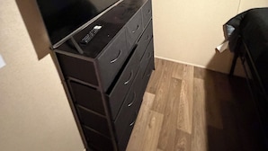 Una stanza con una TV a schermo piatto su un comò, un letto e un pavimento in legno.