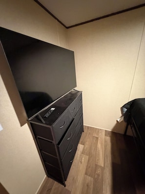 A room with a flat-screen TV on a dresser, a bed, and a wooden floor.