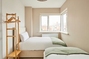 A bedroom with a bed, a wooden hanger rack, a window, and a radiator.