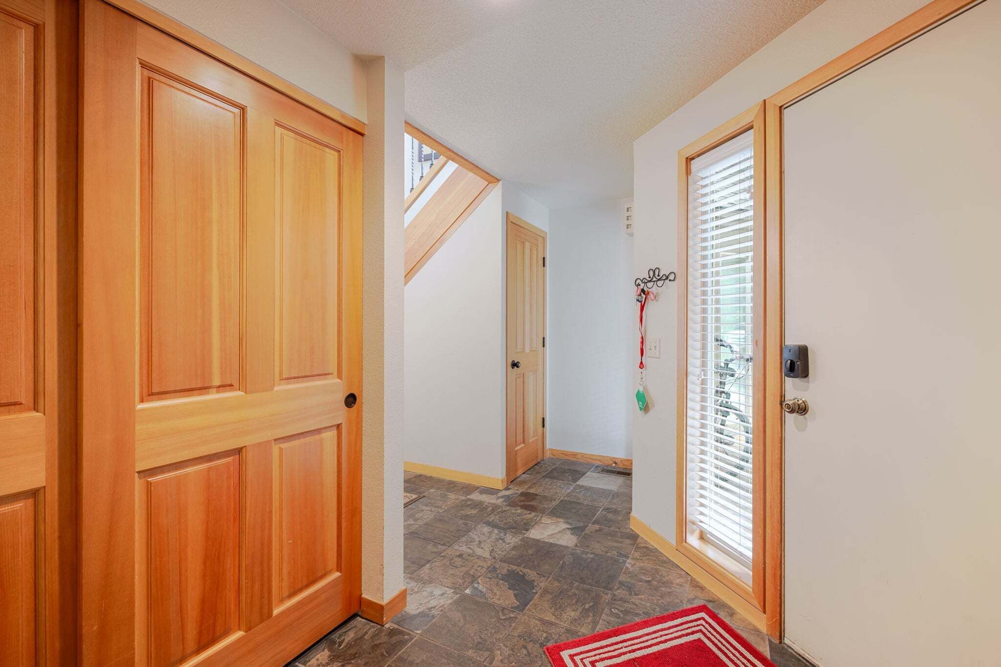 A hallway with wooden doors, a tiled floor, and a red rug.