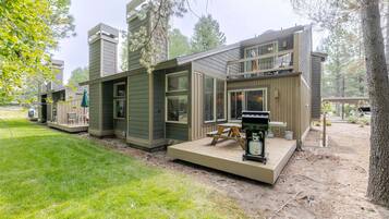 A modern multi-story house with a deck, outdoor seating, and a grill area.