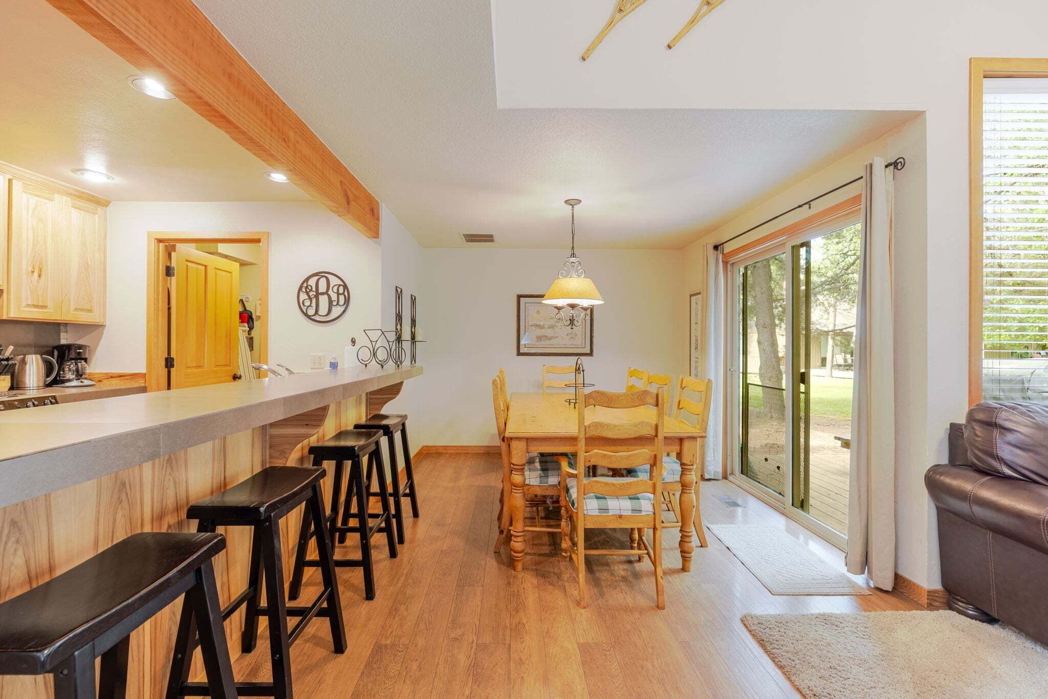 A kitchen with wooden cabinets, a bar stool seating area, a dining table with chairs, and a large sliding glass door leading to an outdoor area.
