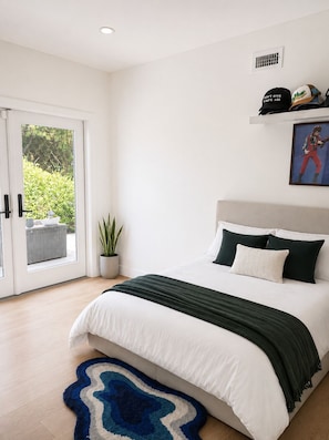 A bedroom with a bed, a potted plant, a door leading to a balcony, and a framed picture on the wall. - Charming Modern House in Los Angeles, Walkable and Quiet (Los Angeles)