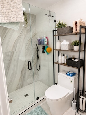 A modern bathroom with a glass shower enclosure, a toilet, and a shelf with toiletries. - Charming Modern House in Los Angeles, Walkable and Quiet (Los Angeles)
