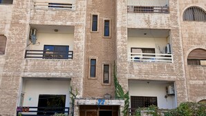 Um edifício de vários andares com entrada central, diversas varandas e um número '72' sobre a porta.
