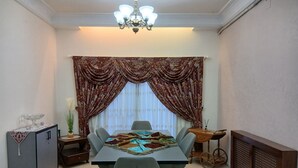 Uma sala de jantar com uma mesa posta para quatro pessoas, um lustre, um armário e um radiador.