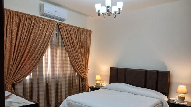 Quarto com cama, cortinas, mesa de cabeceira, abajur e ar condicionado.