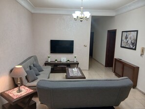 A living room with a grey sofa, a coffee table, a TV mounted on the wall, a chandelier, and a framed artwork on the wall.