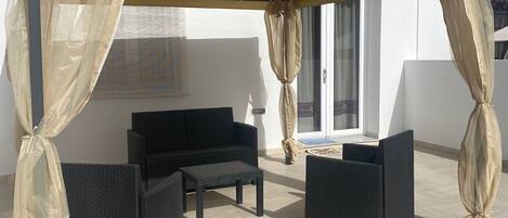 An outdoor patio with a covered seating area, including a sofa and two chairs, and a small table.