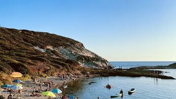 Ein felsiger Strand mit Menschen, Booten und Sonnenschirmen.