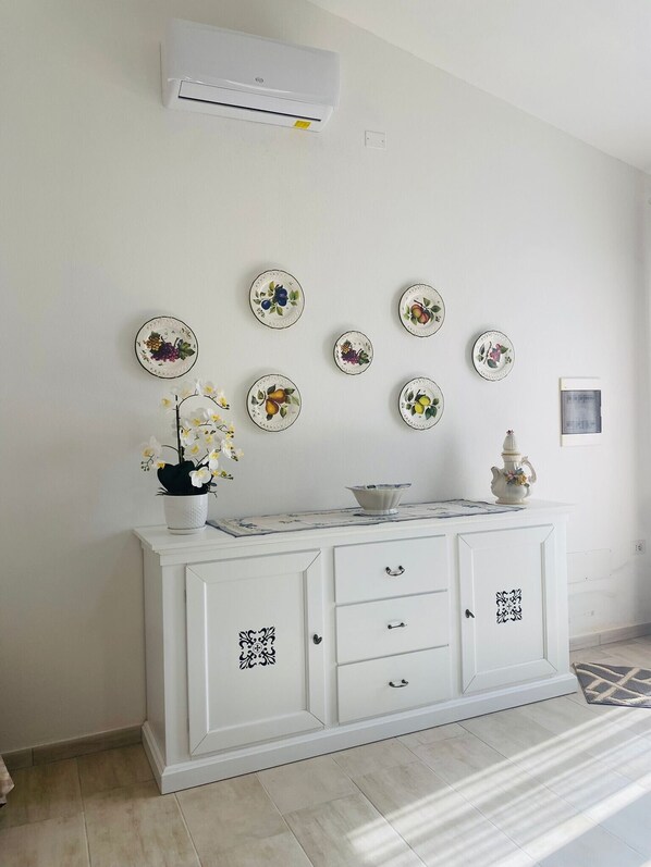A white cabinet with decorative plates, a potted orchid, and a small vase on top.