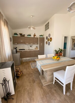 A modern kitchen with wooden cabinets, a dining area with a table and chairs, and a ceiling light fixture.