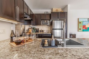 A modern kitchen with dark wood cabinets, stainless steel appliances, a granite countertop, and a coffee machine. - Whole 2BD House – Spectacular Orchard Overlook! (Cawston)