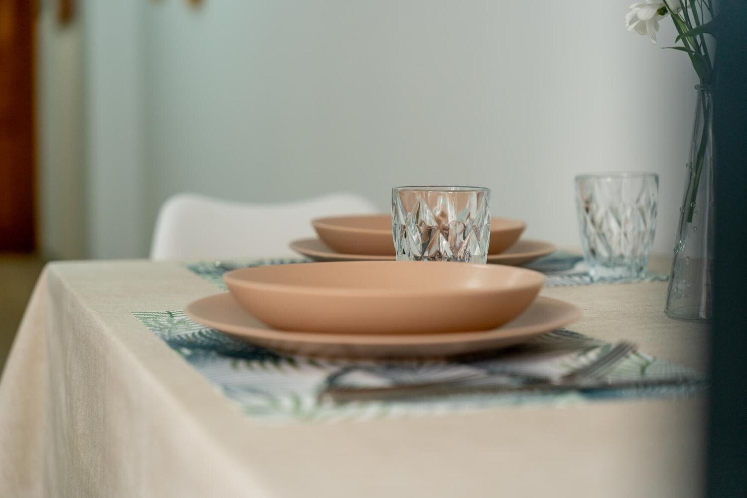 Une table dressée avec des assiettes, des verres et un vase rempli de fleurs.