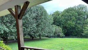 A porch with a wooden railing overlooking a grassy area with trees and a fence.