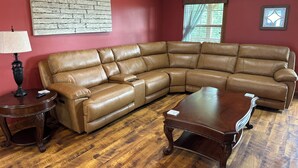 A living room with a brown leather sectional sofa, a wooden coffee table, a lamp, and a wall with a brick pattern.