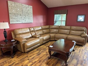 Ein Wohnzimmer mit einem braunen Ledersofa, einem Holztisch, einer Lampe und einer Wand mit Ziegelmuster.