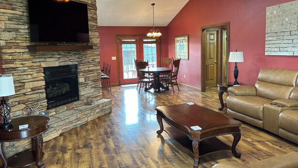 A living room with a stone fireplace, a television mounted above it, a dining area with chairs and a table, and a leather sofa.