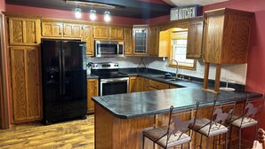 A kitchen with wooden cabinets, a black refrigerator, a microwave, a stove, and a bar area with stools.