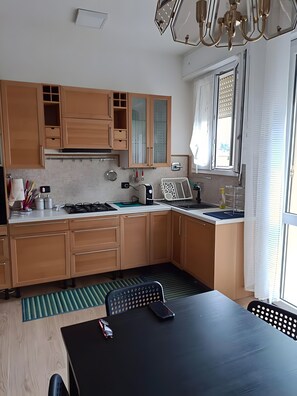 A modern kitchen with wooden cabinets, a gas stove, a sink, and a dining area with a table and chairs.