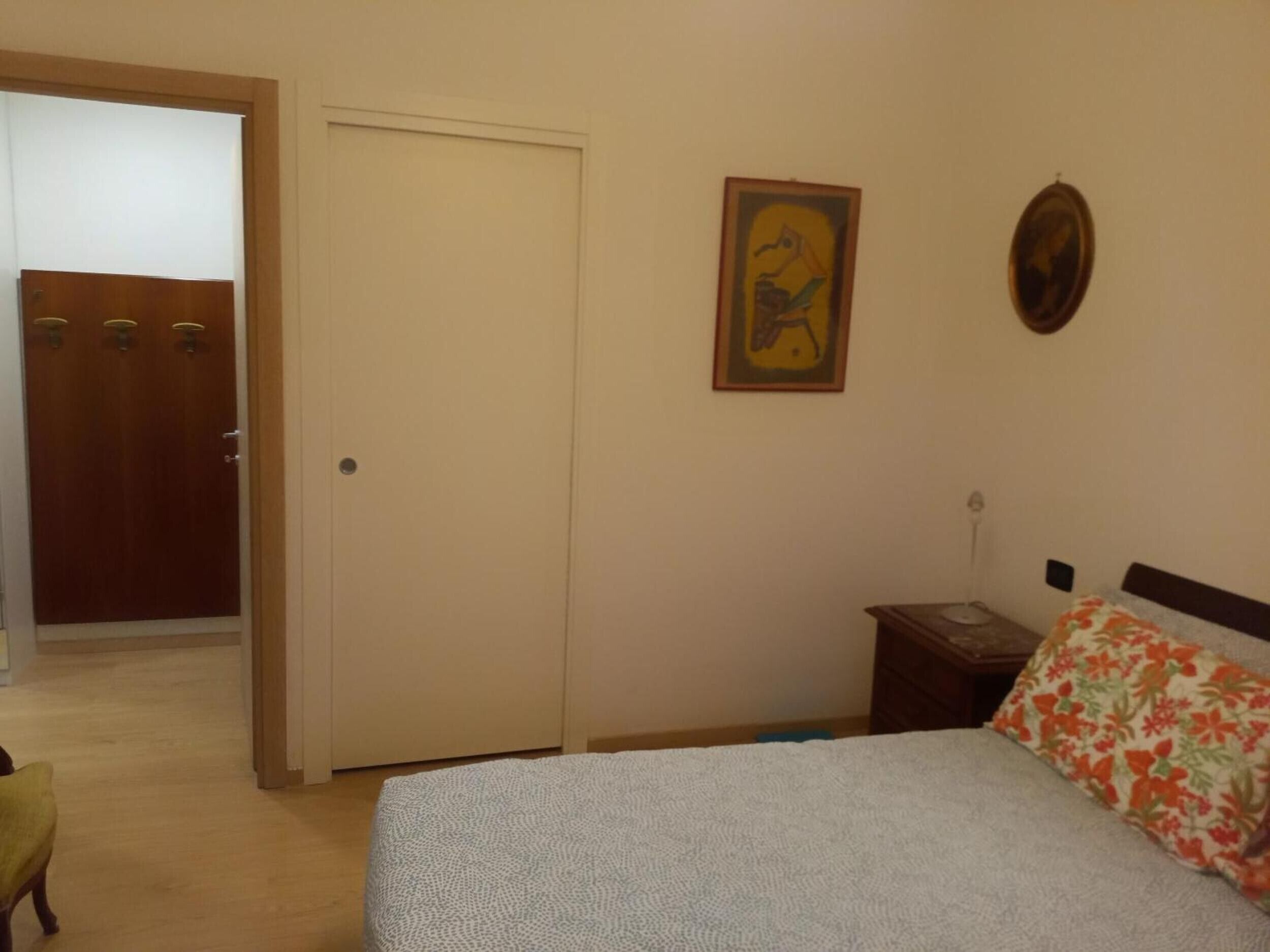 Ein Schlafzimmer mit einem Bett, einem Nachttisch, einer Tür und einer Wand mit einem gerahmten Bild.