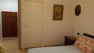 Ein Schlafzimmer mit einem Bett, einem Nachttisch, einer Tür und einer Wand mit einem gerahmten Bild.