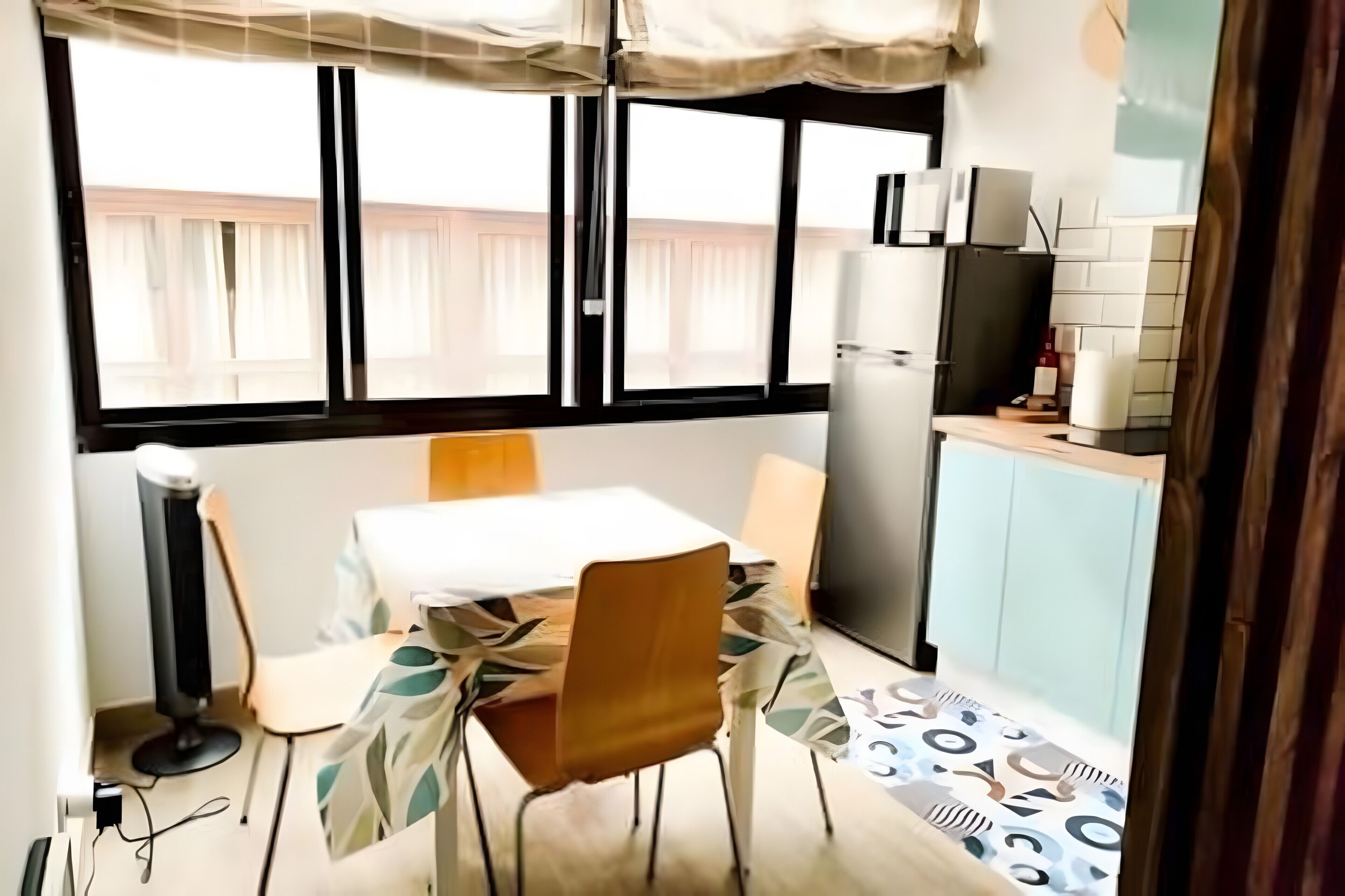 Una cocina pequeña y funcional con comedor, refrigerador y ventana con cortinas.