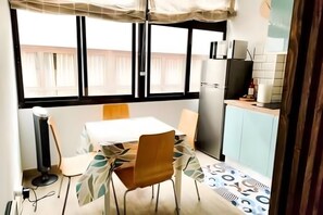 Een kleine, compacte keuken met een eethoek, een koelkast en een raam met gordijnen.