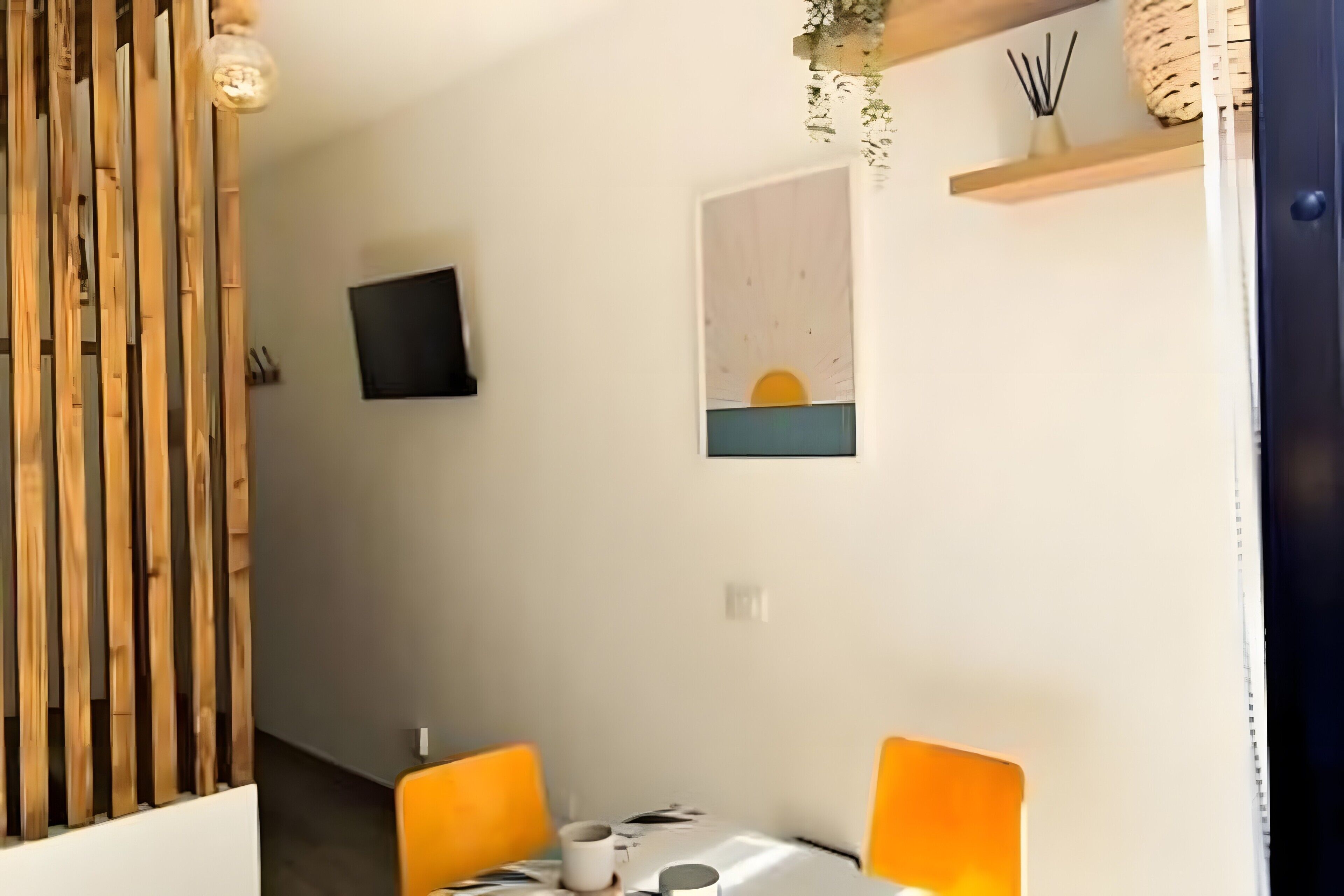 A dining area with a table, chairs, a TV mounted on the wall, and a painting above the table.