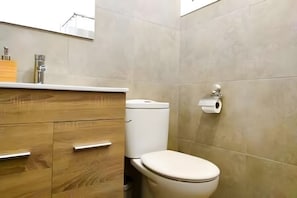 Ein Badezimmer mit Toilette, einem Holzkosmetikschrank und einer Toilettenpapierrolle an der Wand.