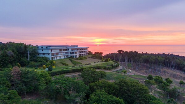 A multi-story building with a landscaped garden and a view of the sunset over the ocean. - jiros garden (Isinomaki)