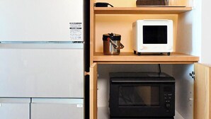 Una cocina compacta con un refrigerador blanco, un microondas sobre la encimera y otro microondas negro dentro de un mueble.