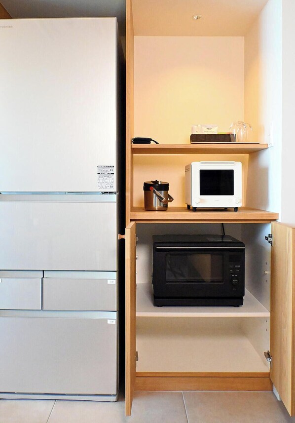 Une cuisine compacte avec un réfrigérateur blanc, un four à micro-ondes posé sur le plan de travail et un autre four à micro-ondes, de couleur noire, rangé dans un placard.