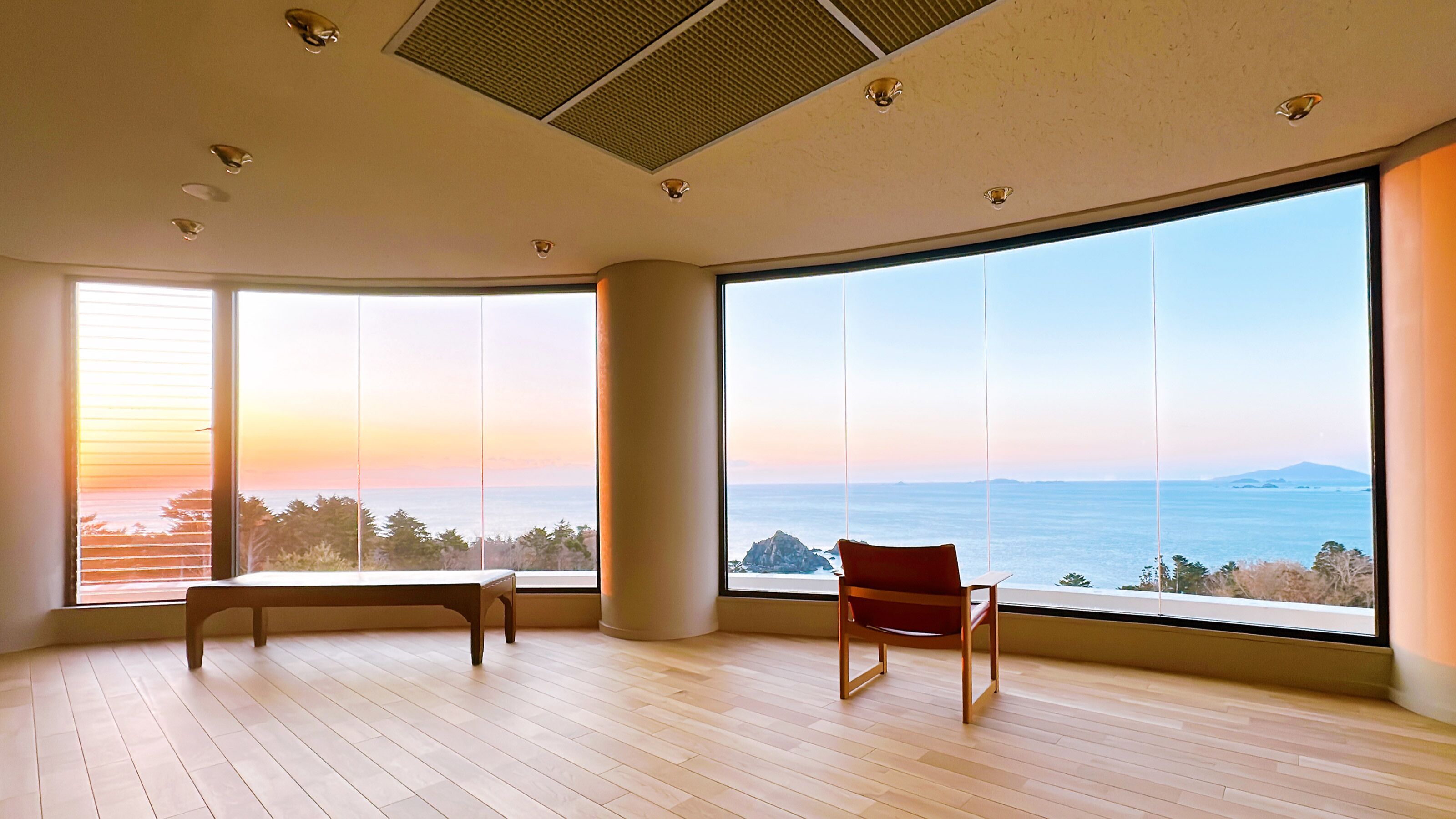 A spacious room with large windows offering a view of the sea and distant land.
