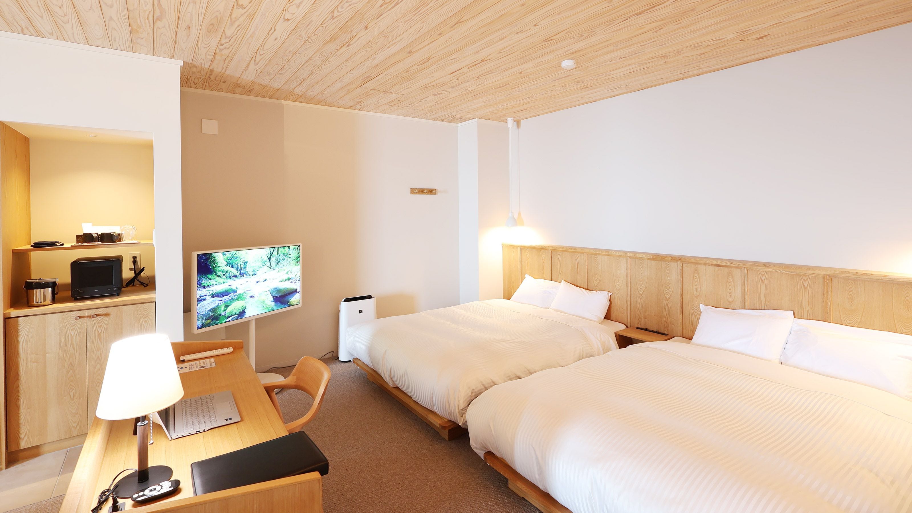 A hotel room with two beds, a desk with a computer, a television, and a kitchenette.