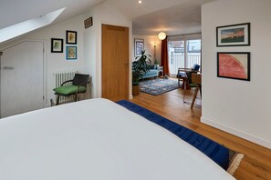 Une chambre comprenant un lit, une chaise, un radiateur et une porte donnant sur un espace de vie avec un canapé, une table et une plante.