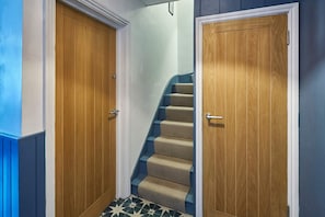 Ein Flur mit zwei Holztüren, einer mit blauem Teppich belegten Treppe und einem gefliesten Boden.