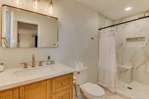 Ein Badezimmer mit einem weißen Waschbecken, goldenen Armaturen, einem Spiegel, einer Toilette und einer Dusche mit Glastür.