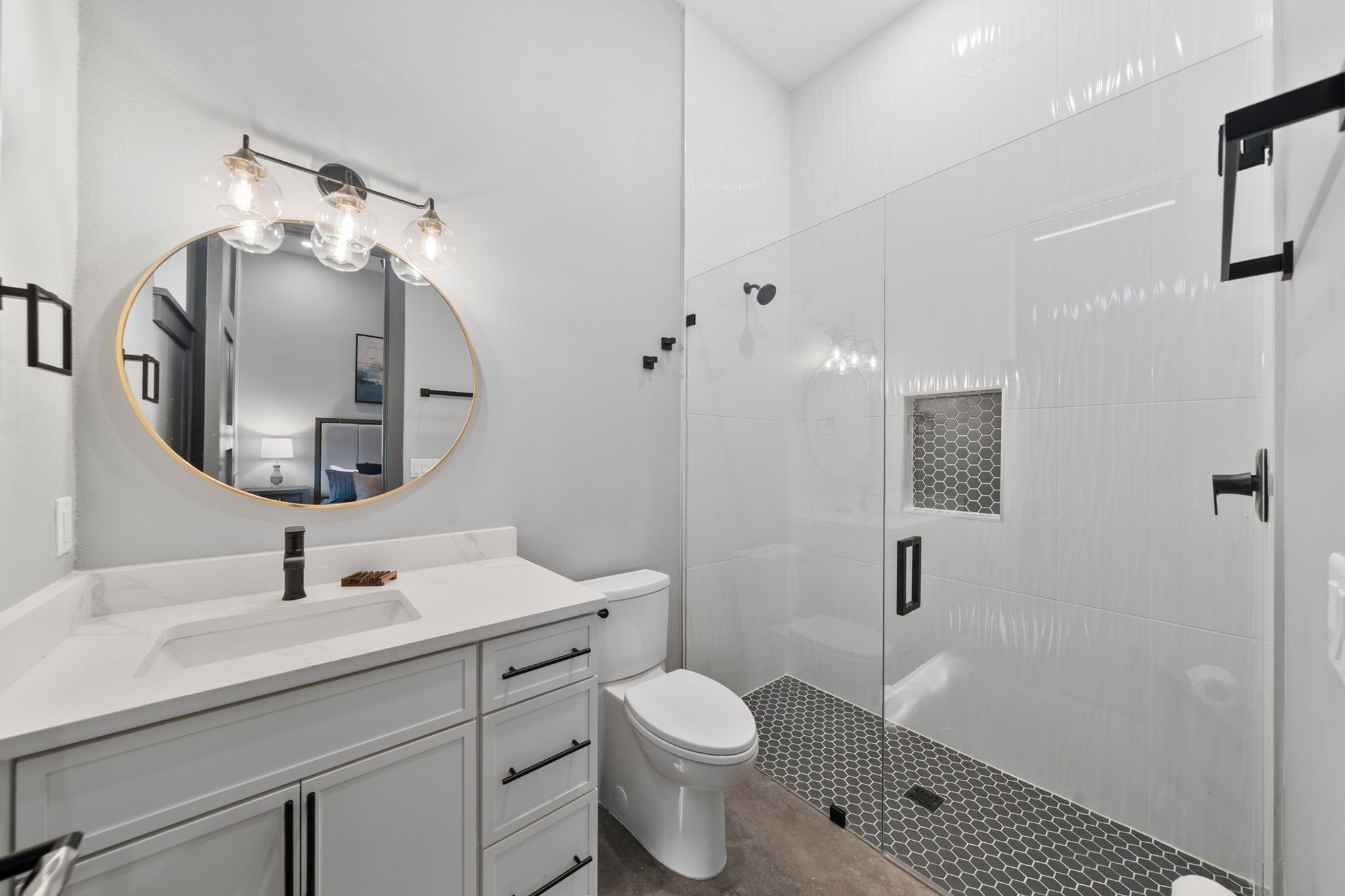 A modern bathroom with a round mirror, a toilet, a shower with glass doors, and a tiled floor.