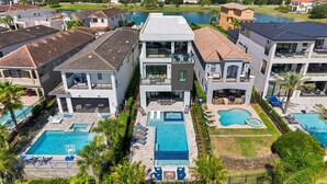 A residential complex with multiple houses, a central swimming pool, and a lake in the background. - WOW Home with Arcade Floor + Theater | Private Pool & Spa (Kissimmee)