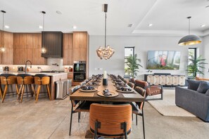 A modern kitchen with wooden cabinets, a central island, and a dining area with a long table and chairs. - WOW Home with Arcade Floor + Theater | Private Pool & Spa (Kissimmee)