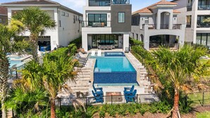 A modern multi-story building with a central pool, outdoor seating, and surrounding greenery. - WOW Home with Arcade Floor + Theater | Private Pool & Spa (Kissimmee)
