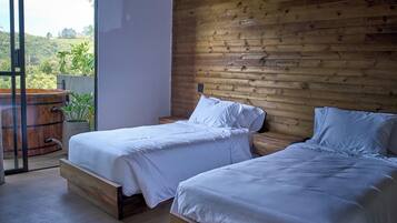 A bedroom with two beds, wooden walls, and a view of greenery outside.