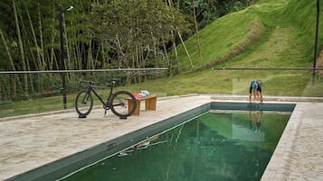 Una piscina con una bicicleta estacionada cerca, rodeada de vegetación.