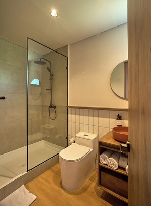 A modern bathroom with a glass-enclosed shower, a white toilet, and a wooden vanity with a round mirror. - Lagoa by Loop (Peñol)